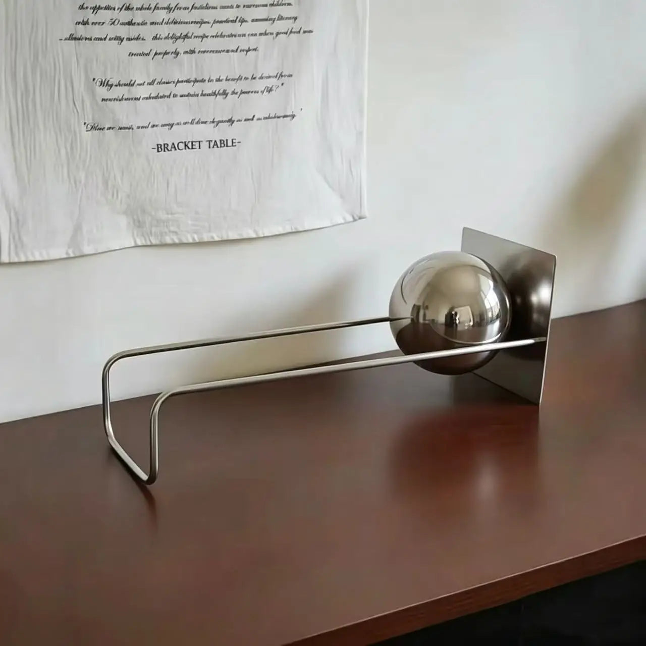 Modern metal desktop bookshelf with silver decorative sphere holding books on a contemporary white desk.