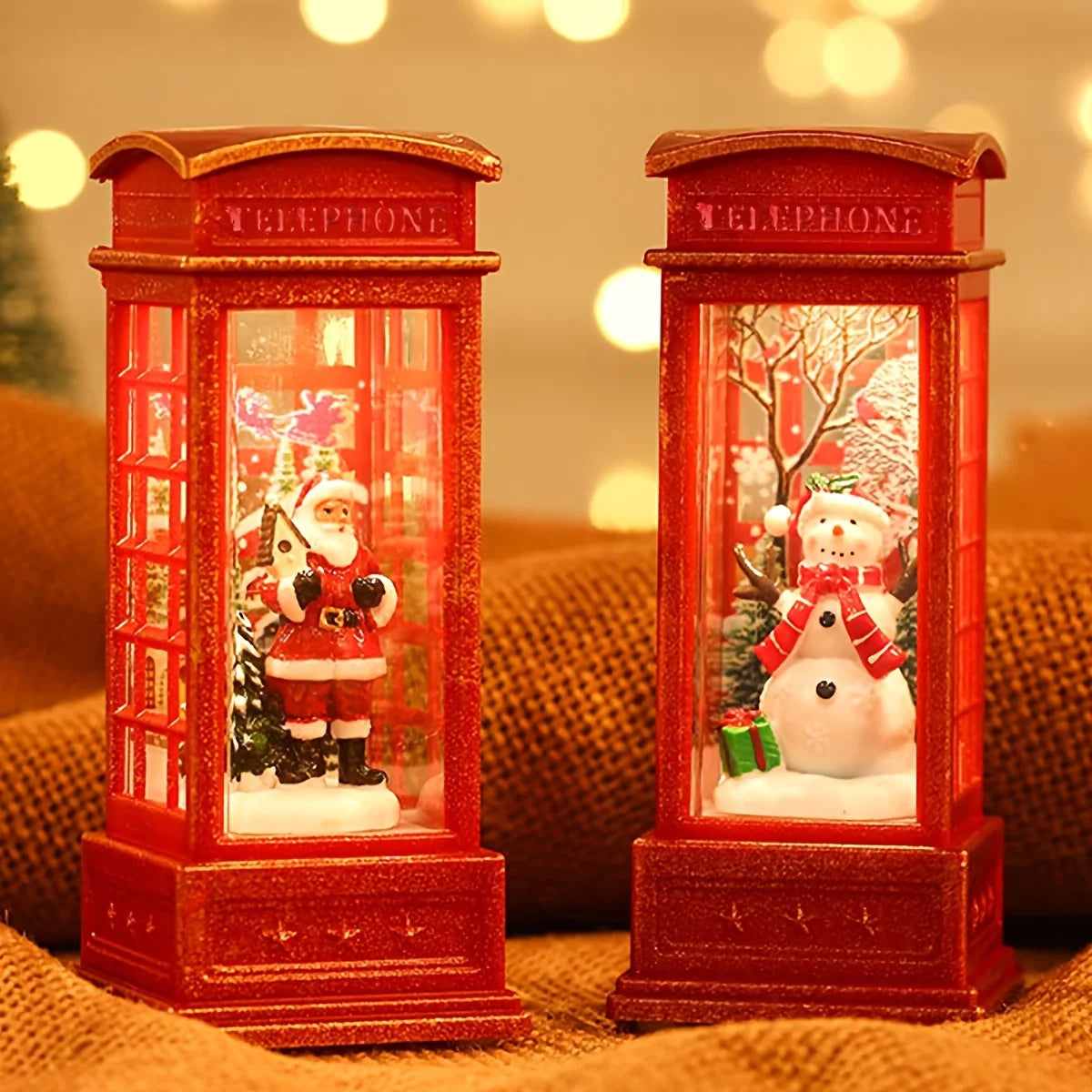 Two red telephone booth snow globes with Santa and snowman figures inside, on a textured surface.