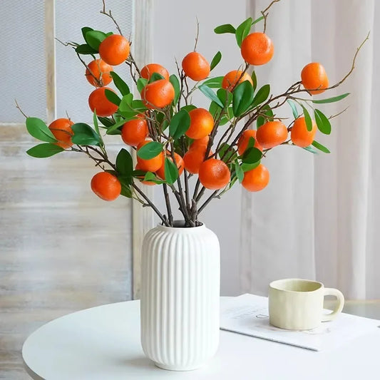 Vase with artificial orange branches on a table with a cup