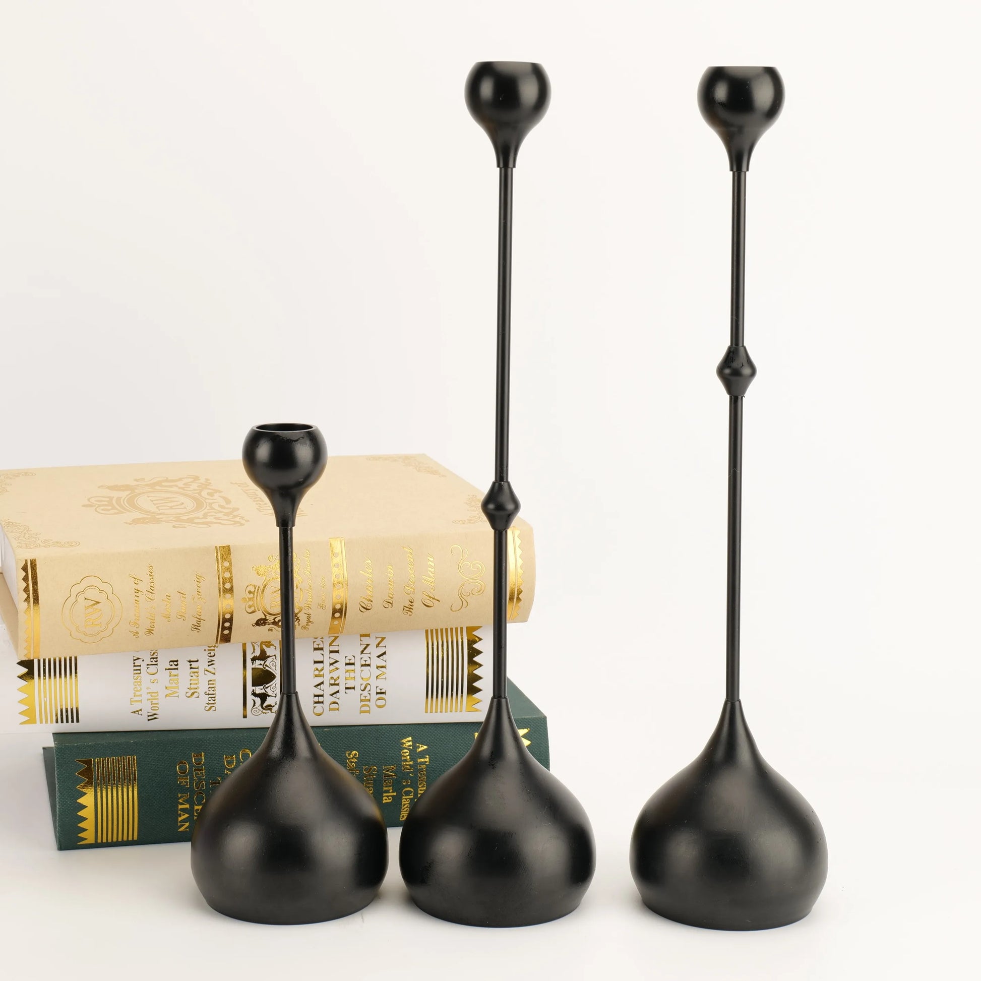 Set of three black decorative vases on a white background with books underneath.
