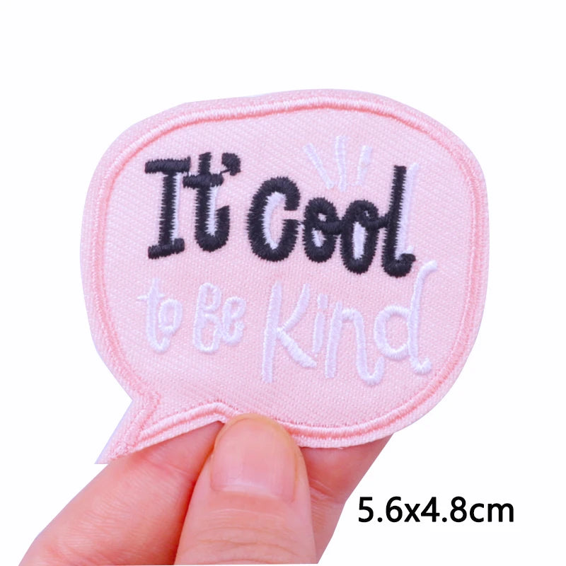 Pink speech bubble patch with 'It's Cool to be Kind' text held by a hand on a white background.