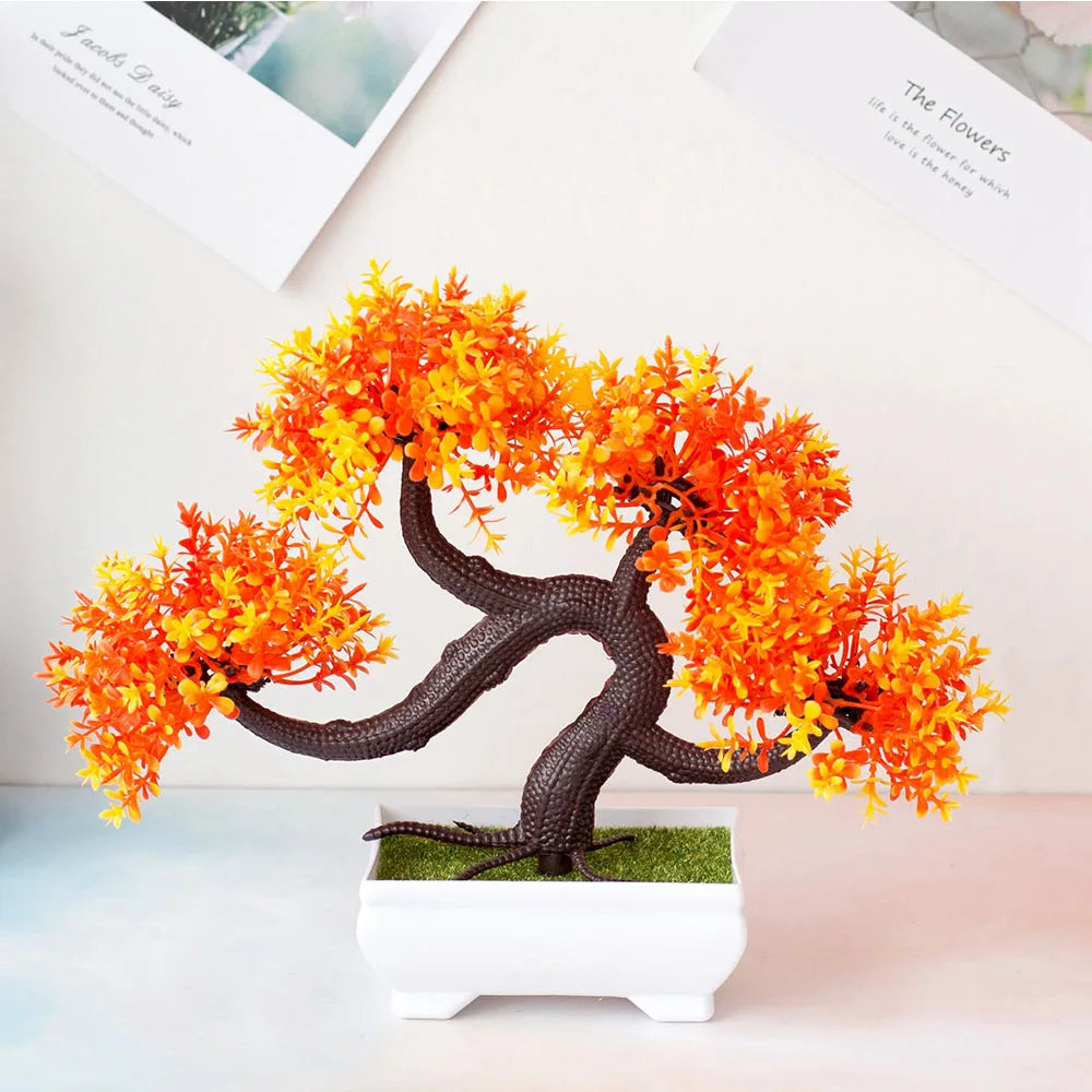 Artificial bonsai tree with orange and yellow leaves on a white surface.