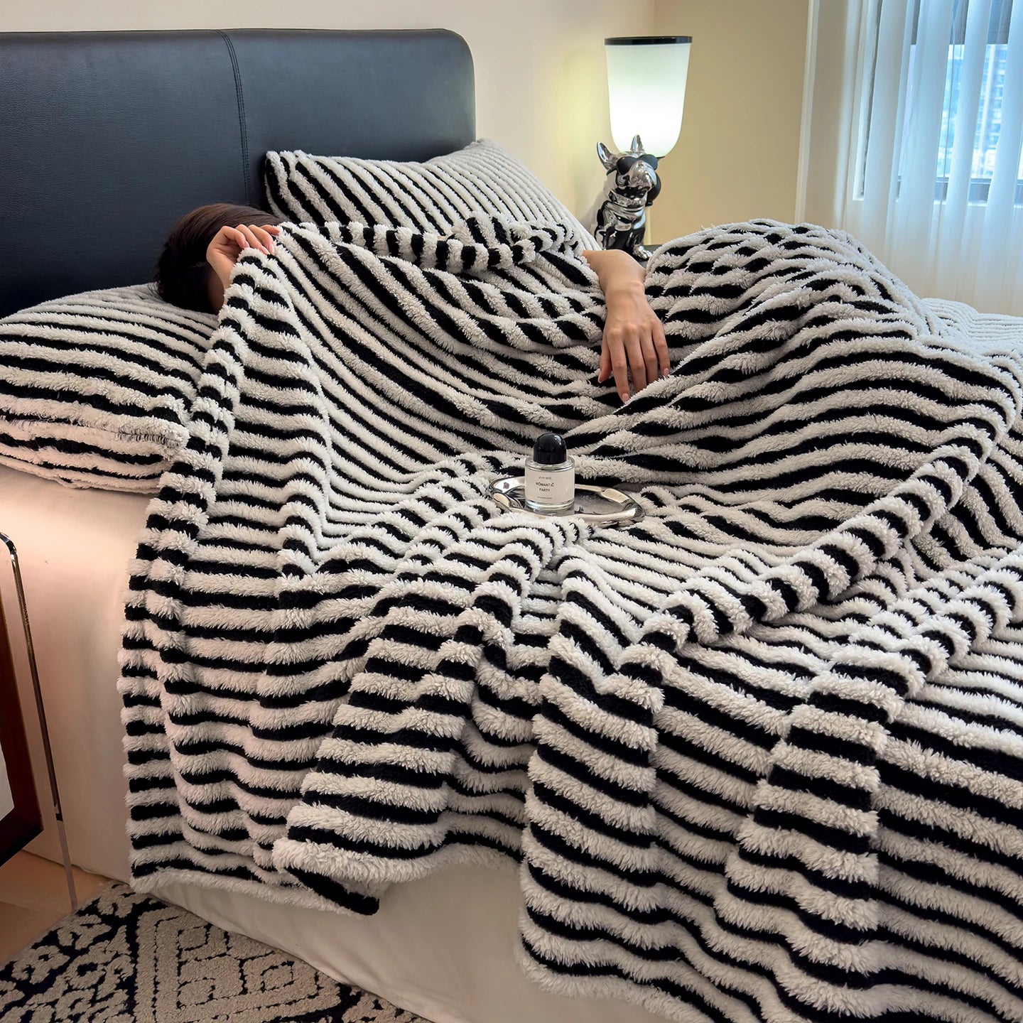 Person lying on a bed under a black and white striped blanket