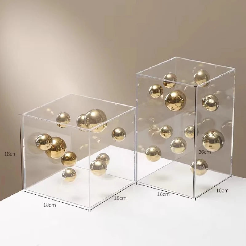Two clear acrylic boxes with gold spherical objects inside, on a neutral background.