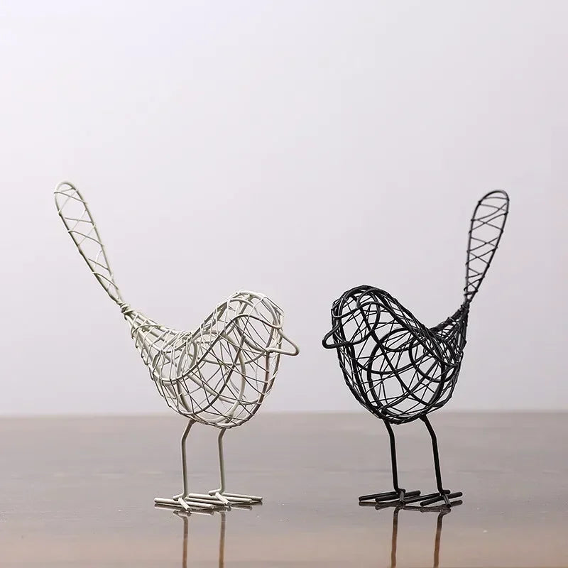 Two wire bird sculptures, one white and one black, on a reflective surface with a light gray background.
