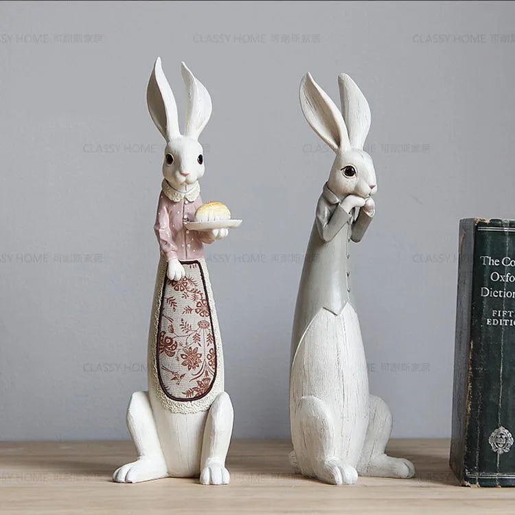 Two decorative rabbit figurines on a wooden surface with a book in the background.