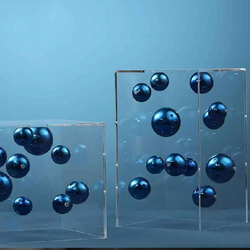 Blue metallic-finish spheres suspended within two transparent acrylic cube sculptures.