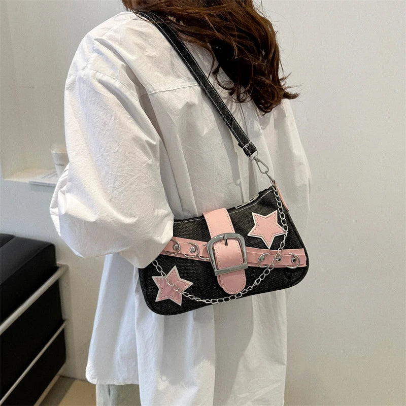 Person holding a black handbag with pink star designs and a silver buckle.