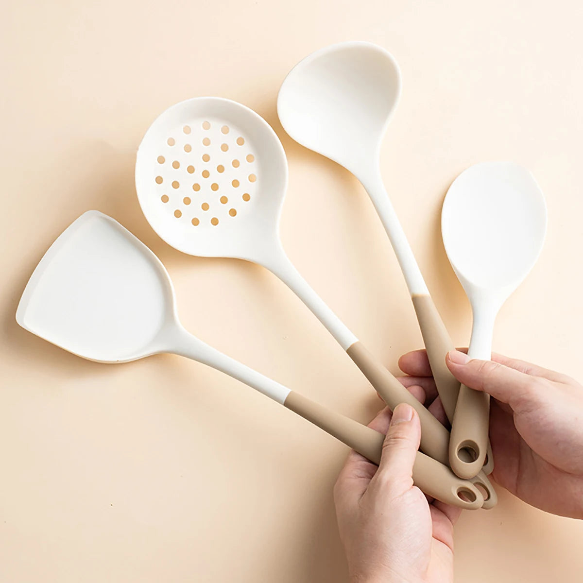 Set of white kitchen utensils including a spatula, ladle, and spoon held by hands on a beige background.