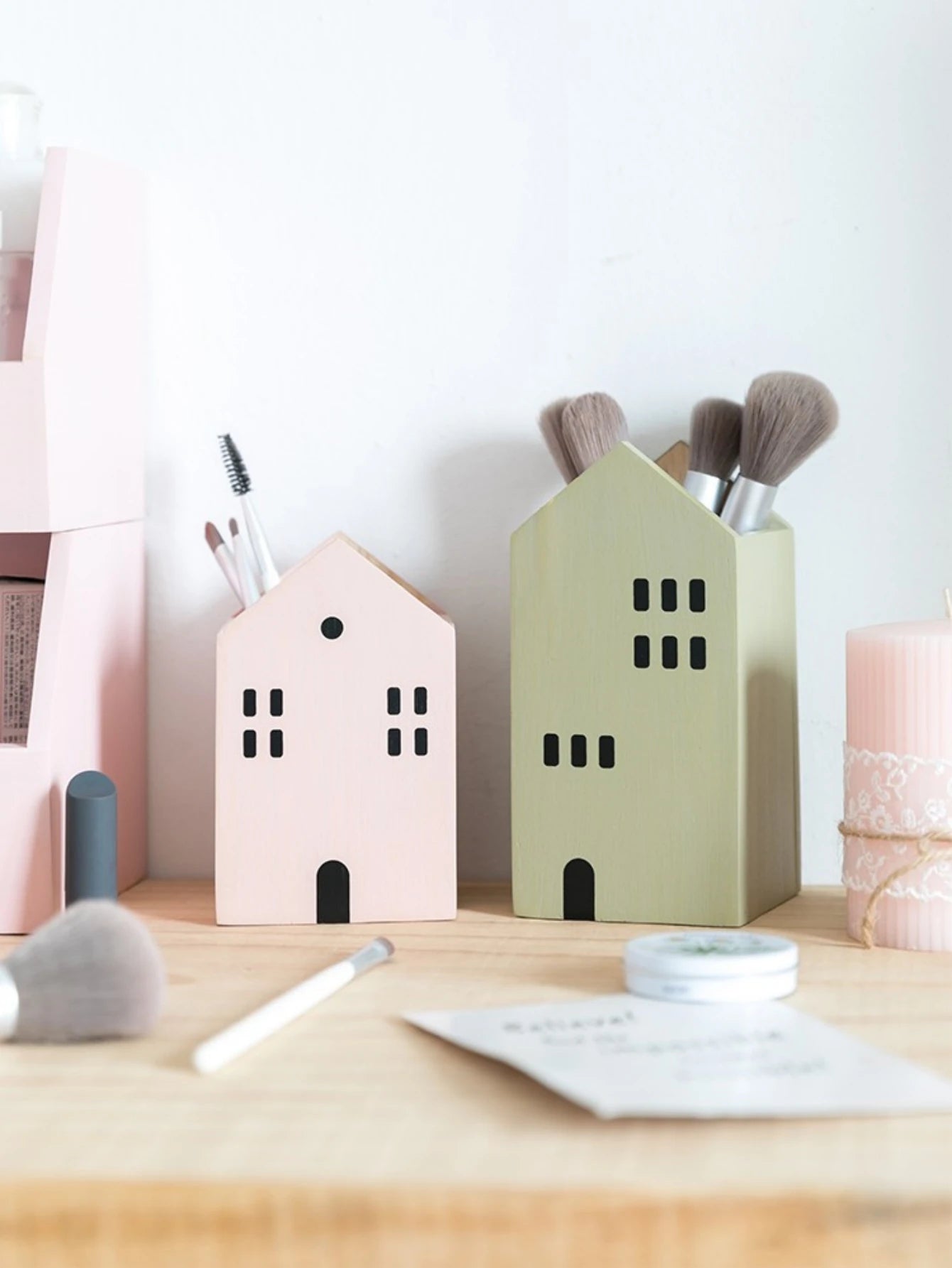 House-shaped makeup brush holders on a desk with stationery items.