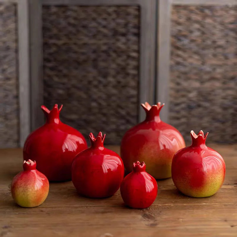 Set of red ceramic pomegranates on a wooden surface with a textured wall background.