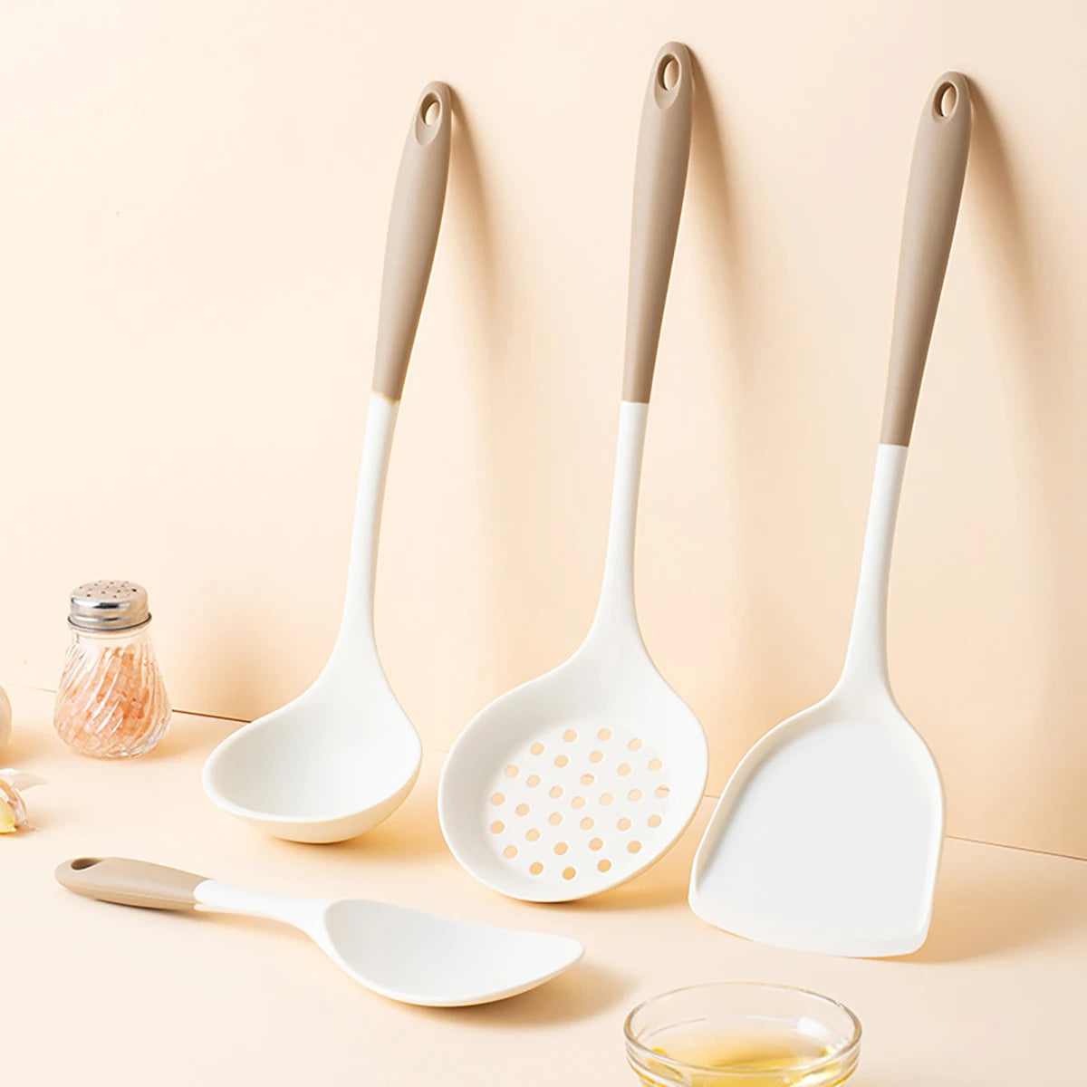 Set of kitchen utensils including a ladle, spatula, and skimmer on a beige background.