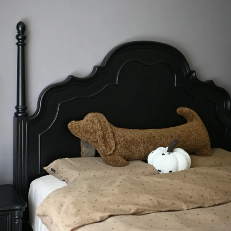 Bed with black headboard, brown dog-shaped pillow, and white pumpkin on beige bedding.