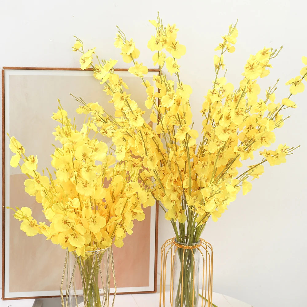 Yellow flowers in vases on a white surface with a framed picture in the background