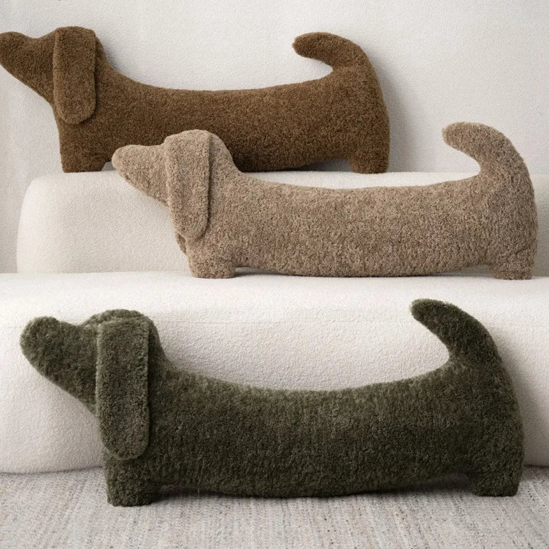 Three dachshund-shaped cushions in different colors on a white surface.