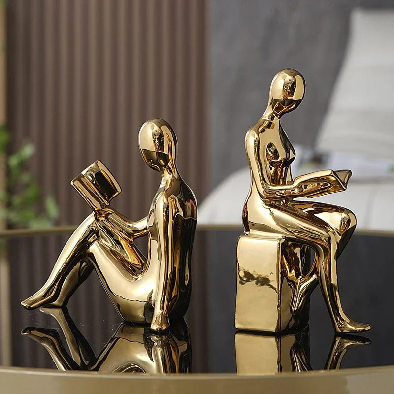 Gold ceramic abstract reading couple bookends displayed on a reflective surface