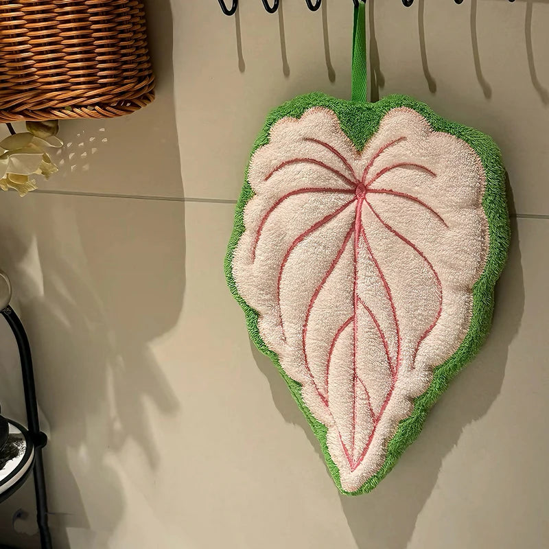 Leaf-shaped towel with pink center and green border on a tiled floor.