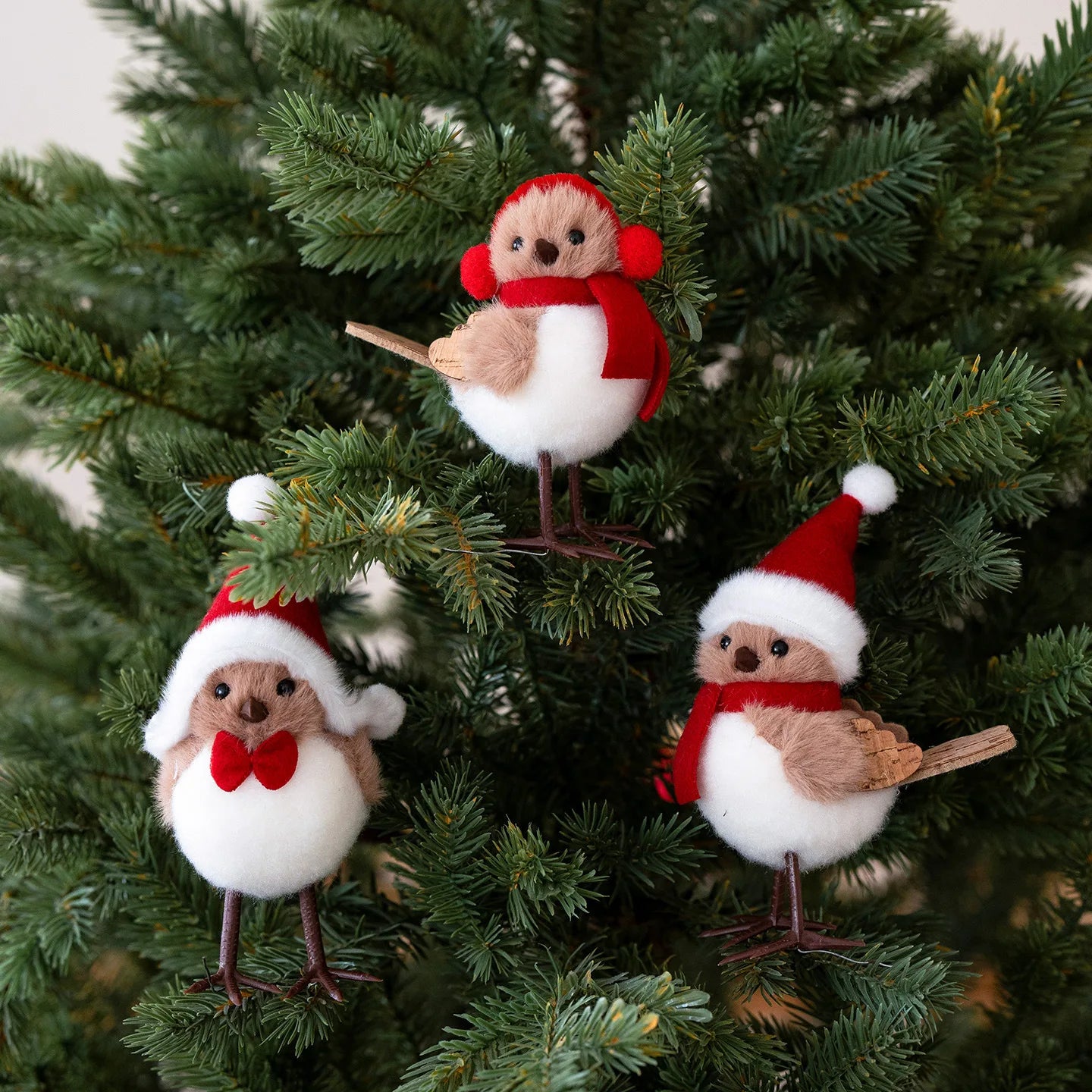 Three festive bird ornaments in red and white hats on a Christmas tree.