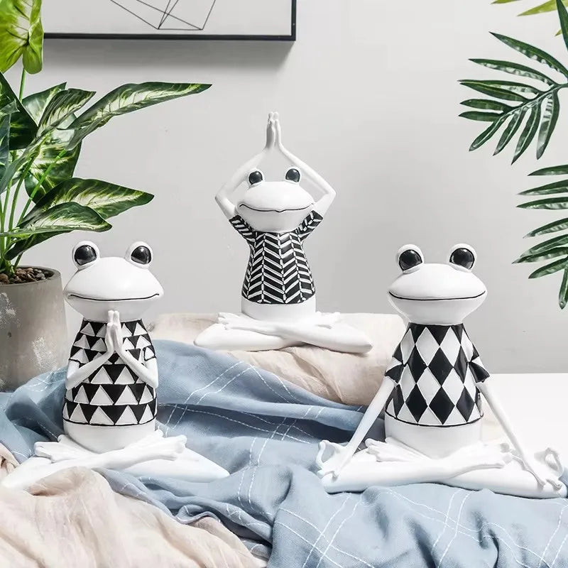 Three frog-shaped figurines in black and white patterns on a bed with plants in the background