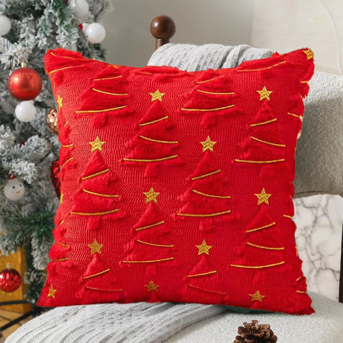 Red pillow with gold tree patterns and stars on a couch next to a Christmas tree.