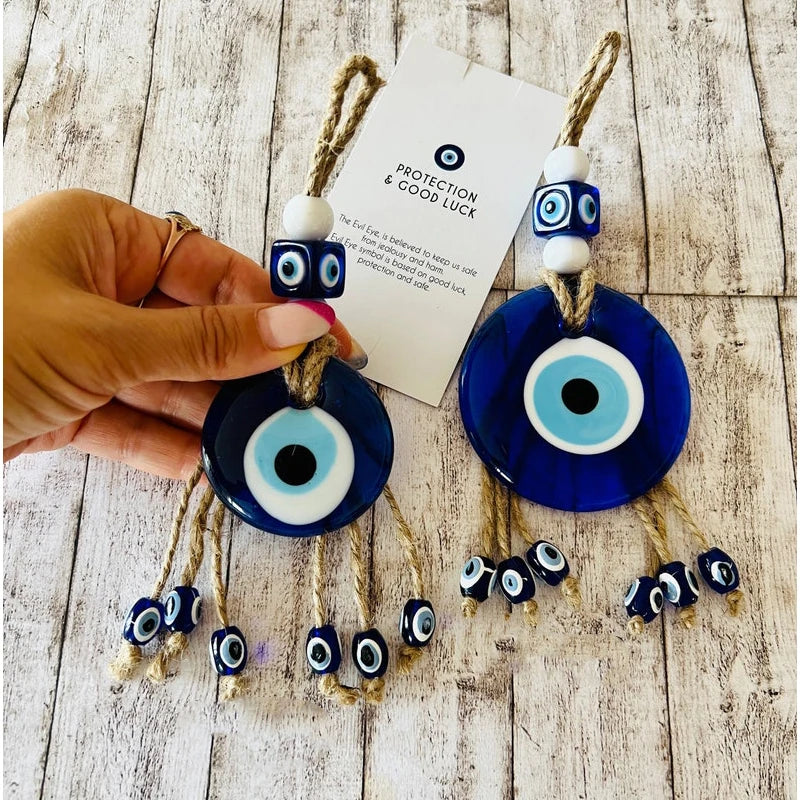 Two blue evil eye ornaments with a hand holding one, on a wooden surface.