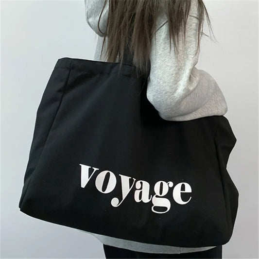 Black tote bag with 'Voyage' text worn by a person against a plain background