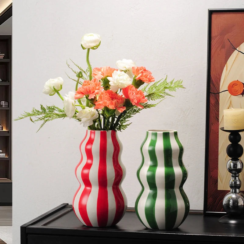 Two wavy-patterned vases with flowers on a shelf against a neutral wall.