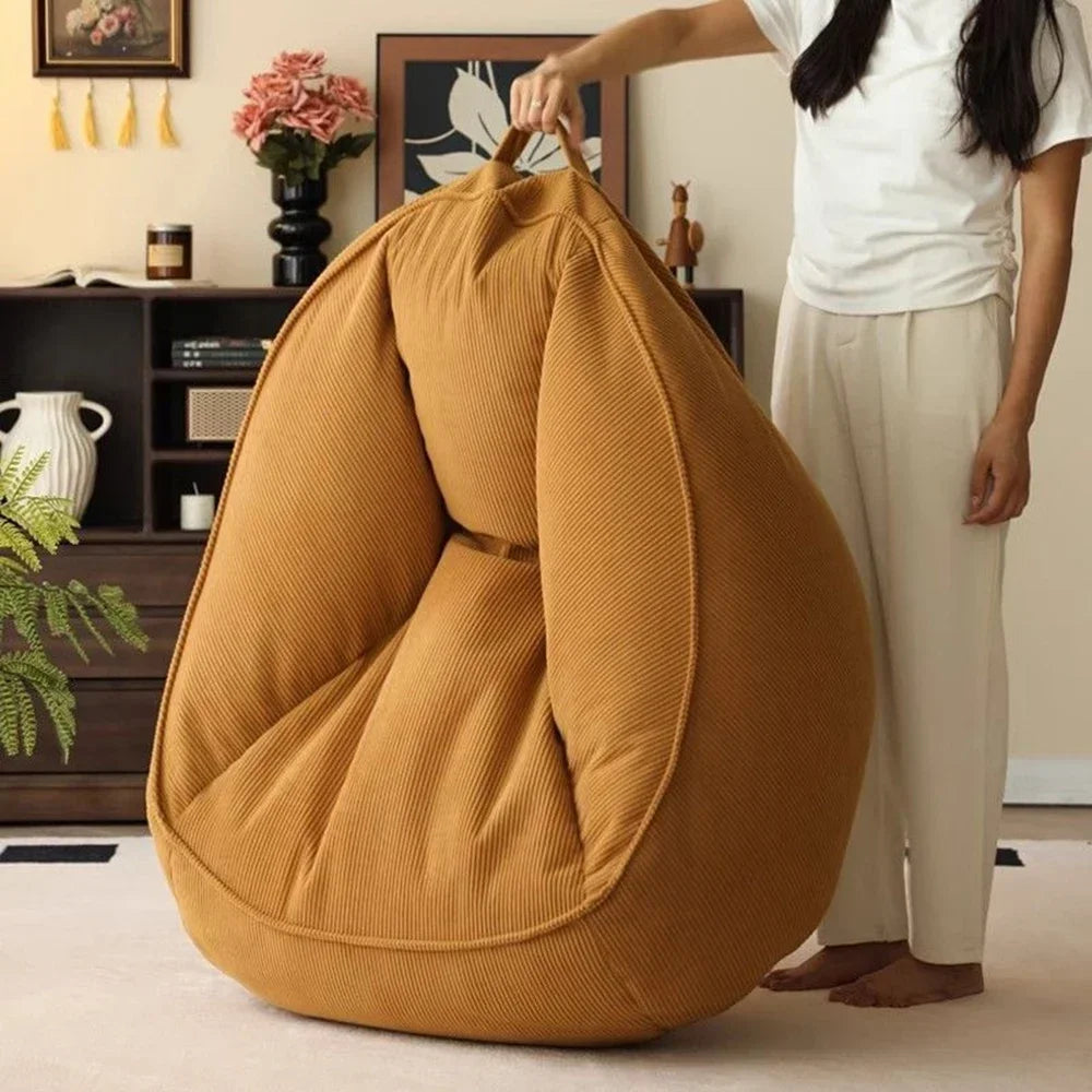 Person holding a mustard yellow bean bag chair in a room with decor elements.
