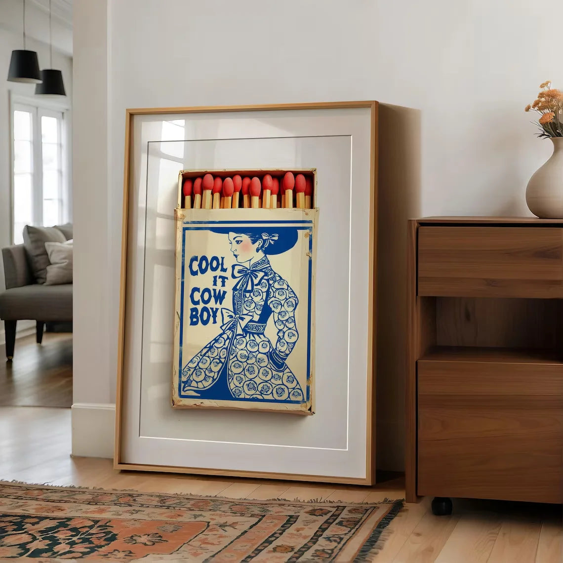 Framed artwork with a matchbox design featuring a cowboy illustration and text in a modern interior setting.