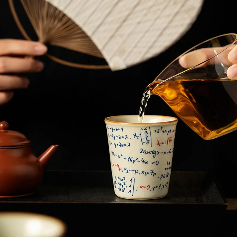 Tea being poured into a cup with mathematical equations, next to a red teapot and a fan.
