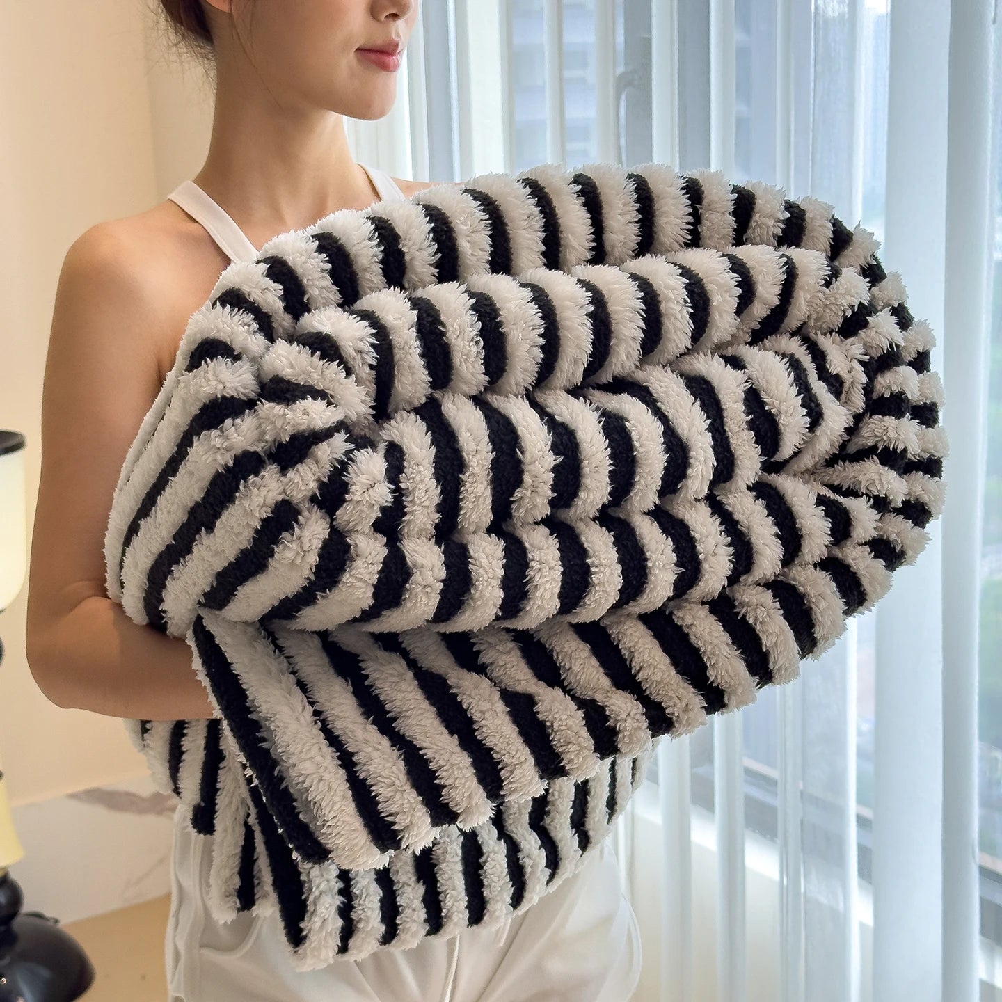 Person holding a black and white striped towel in a bright room with sheer curtains.