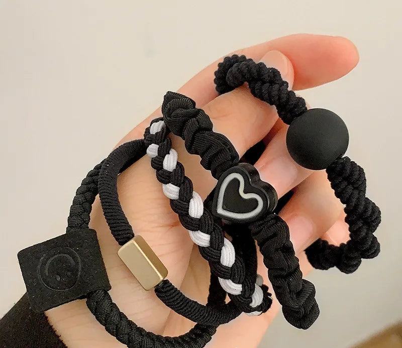 Black braided hair ties with decorative elements held in a hand against a neutral background.