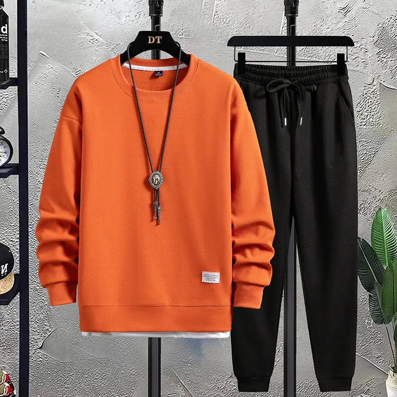Orange sweatshirt and black pants on hangers against a textured wall.