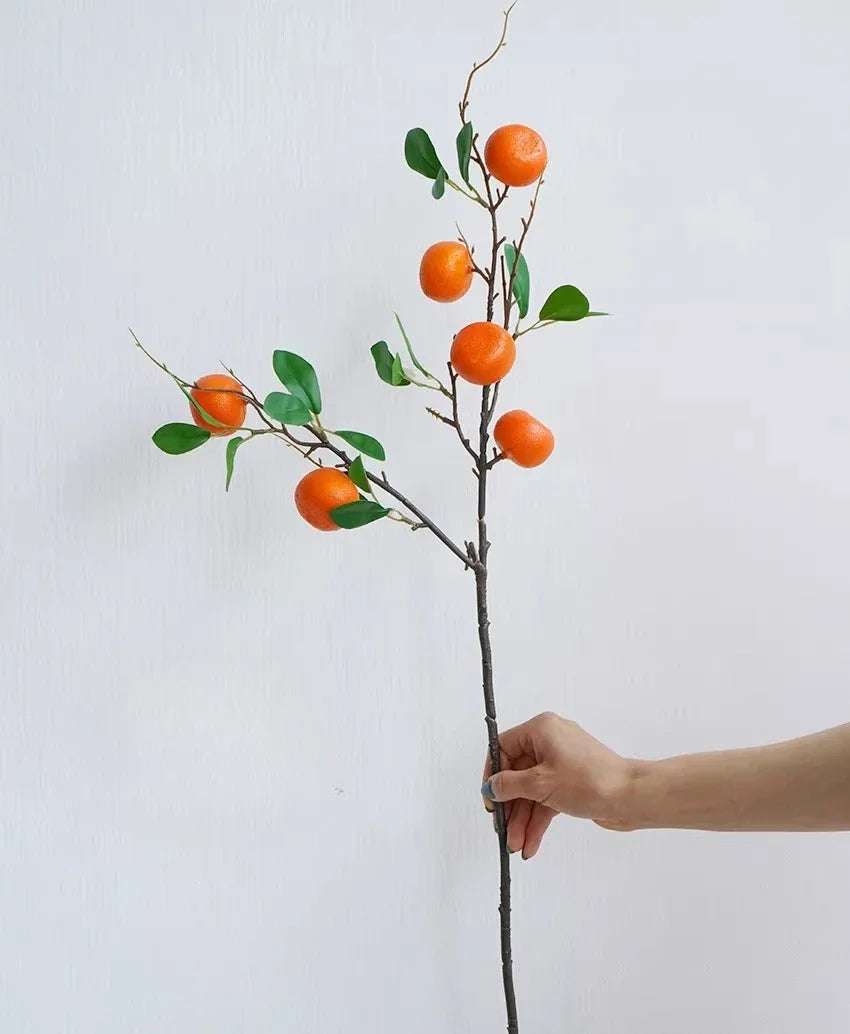 Artificial orange fruit branch held by a hand against a white background