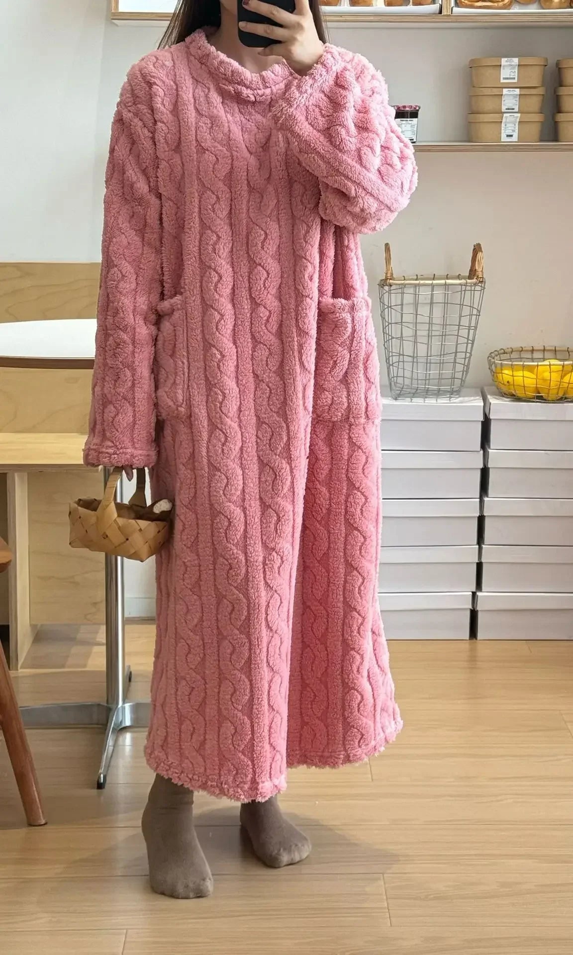 Person wearing a pink cable knit robe in a room with wooden floor and white walls.