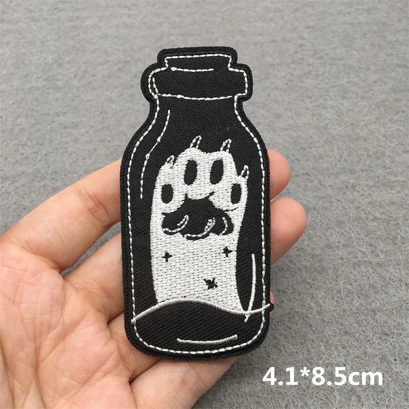 Embroidered patch of a paw print in a bottle held by a hand on a gray background.