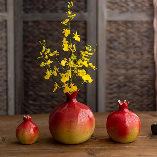 Red pomegranate-shaped ceramic vases in different sizes displayed on a wooden surface