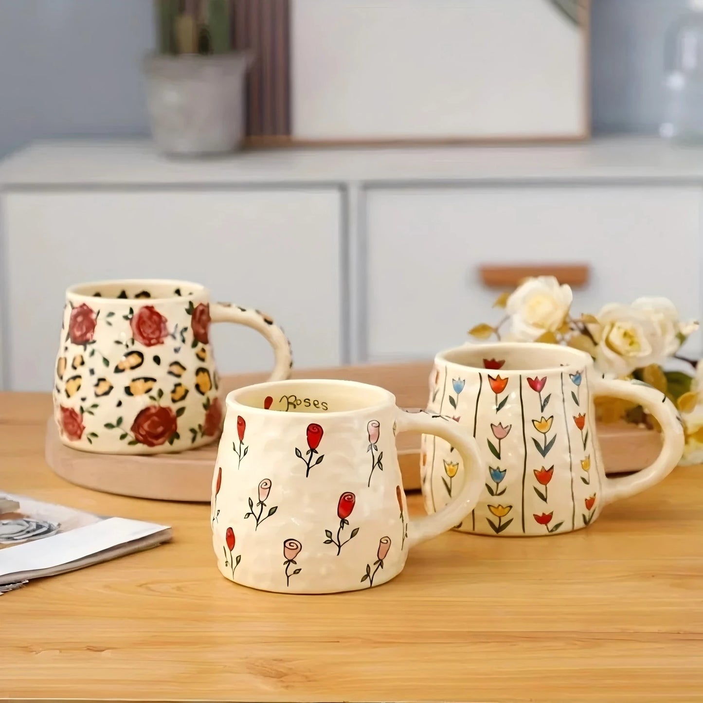 Three ceramic mugs with floral designs on a wooden surface.