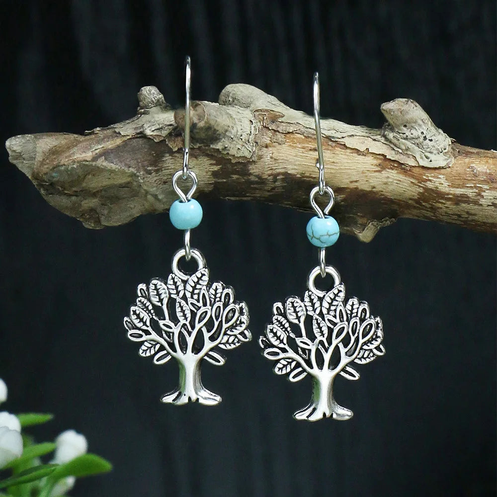 Silver tree-shaped earrings with turquoise beads on a dark background
