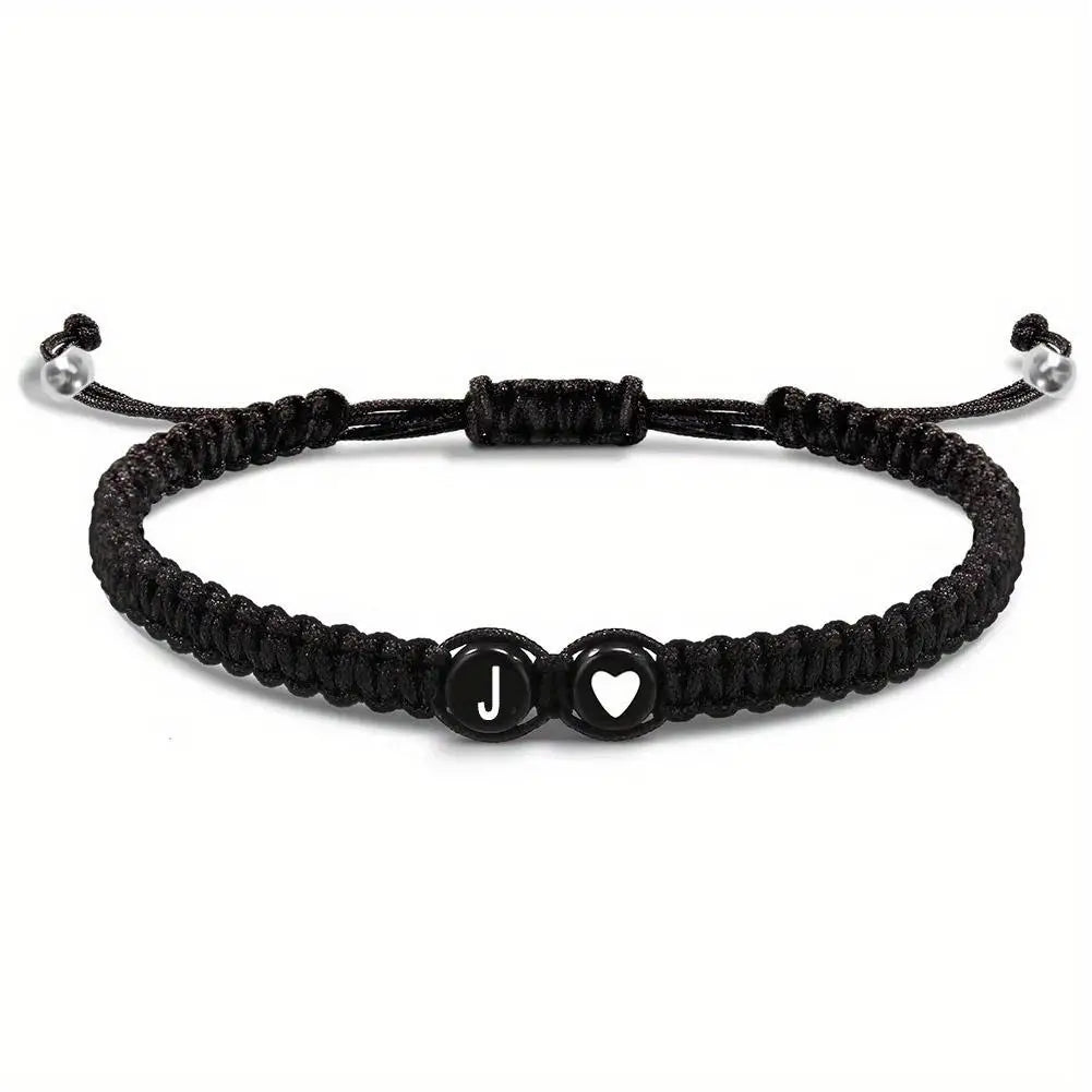 Black braided bracelet with heart and letter 'J' charm on a white background