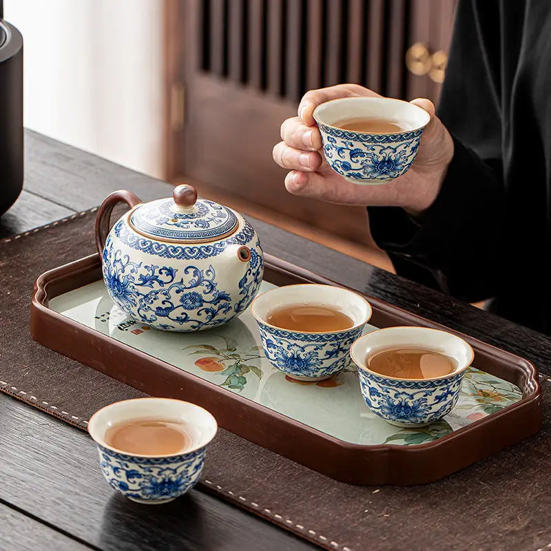 Person holding a blue and white ceramic teacup with a matching teapot and cups on a tray.