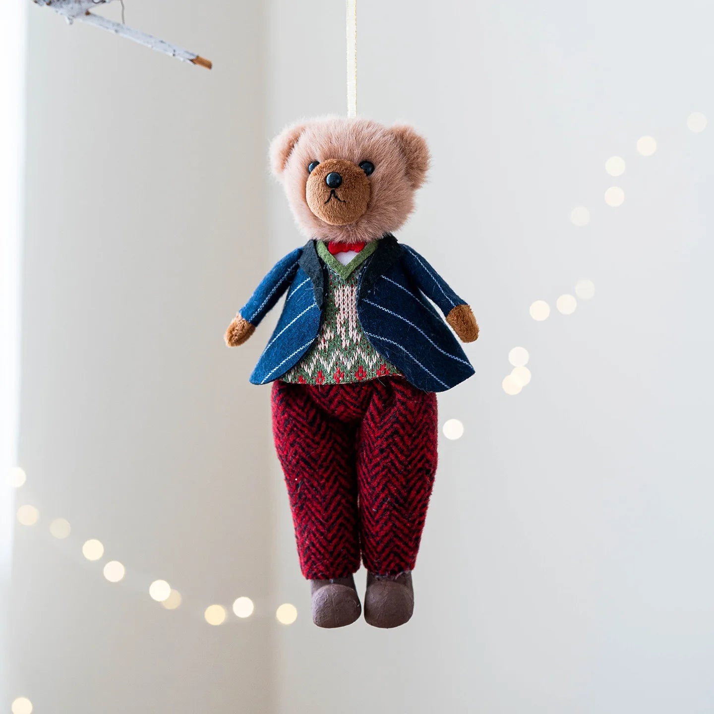 Stuffed teddy bear in a suit hanging against a light background with string lights.