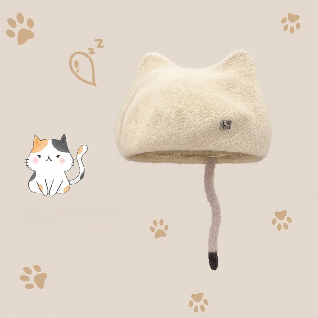 A cream-colored plush cat-ear hat with a long faux-fur tail and a small black brand tag, shown on a beige background with paw-print graphics and a cartoon cat 
