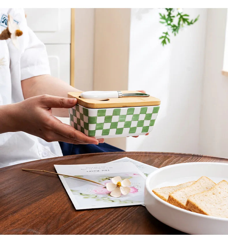 Person holding a green and white checkered container with wooden lid on a wooden table.