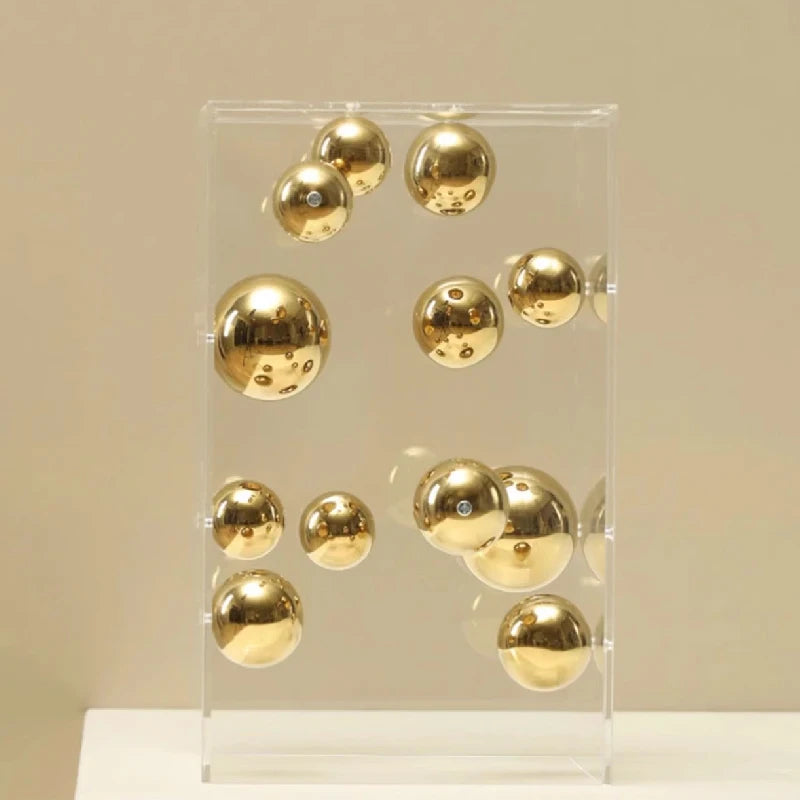 Gold reflective spheres suspended inside a transparent acrylic cube displayed on stacked books.
