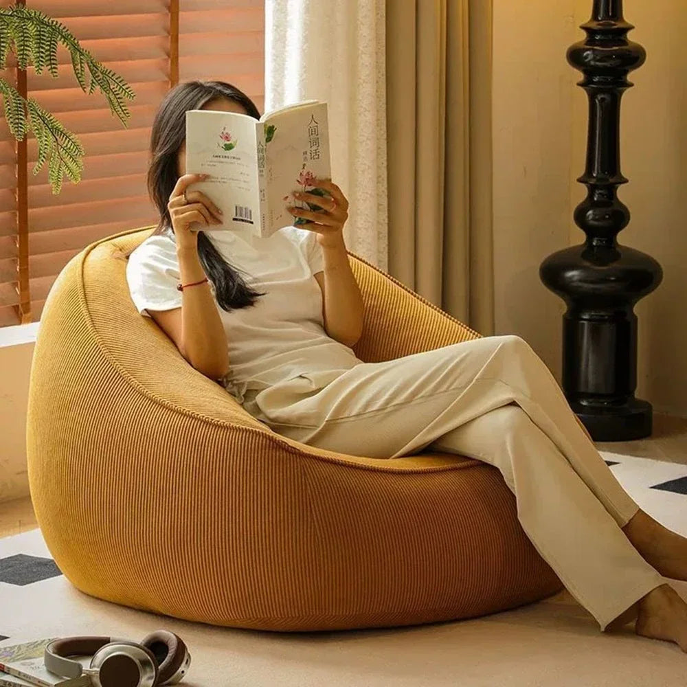 Person reading a book while sitting on a yellow bean bag chair in a cozy room.