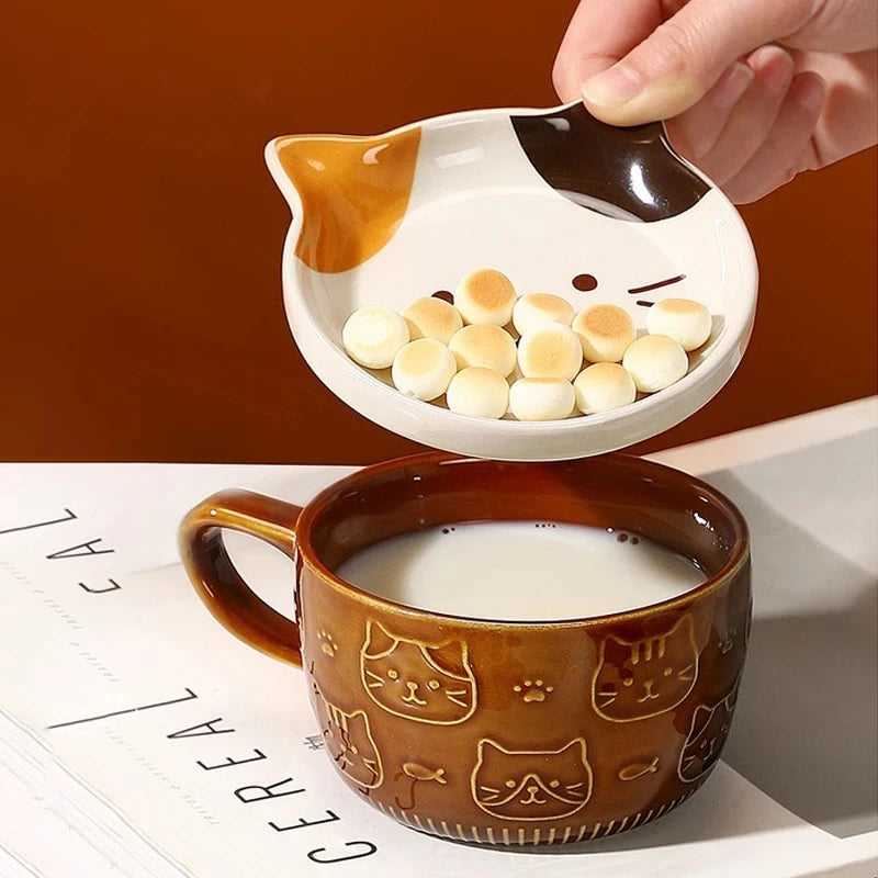 Cat-shaped ceramic bowl being used to scoop cereal into a mug with cat designs.
