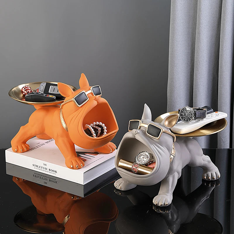 Two dog-shaped jewelry holders, one orange and one gray, on a reflective surface with books underneath.