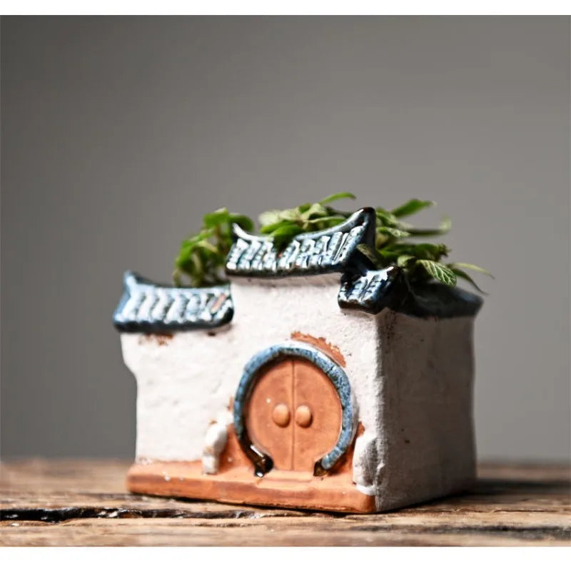 Small ceramic house with a door and greenery on a wooden surface