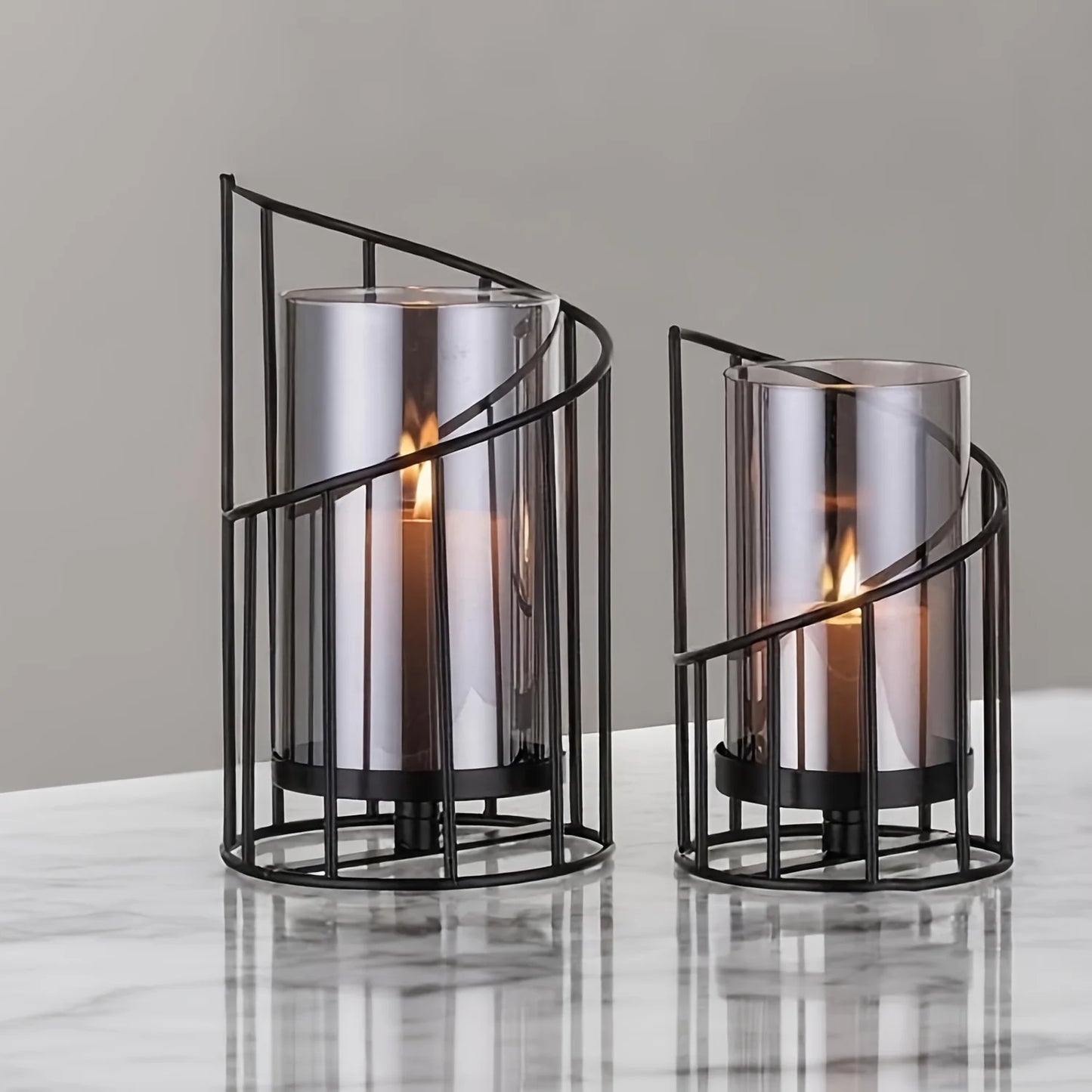 Set of two modern black spiral glass candle holders with smoked hurricane glass displayed on a wooden table in a contemporary home interior.